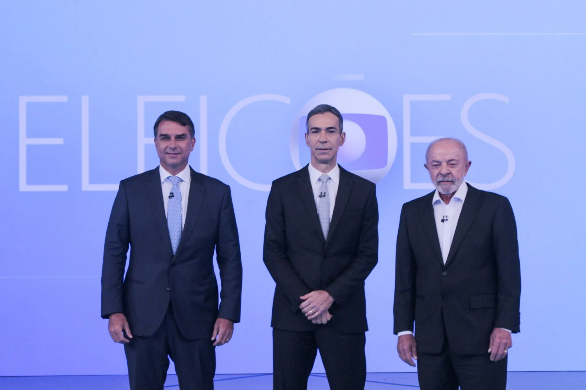 O senador Flávio Bolsonaro (E) e o presidente Luiz Inácio Lula da Silva (D) posam ao lado do jornalista e mediador do debate César Tralli — Foto: Carlos Elias Junior